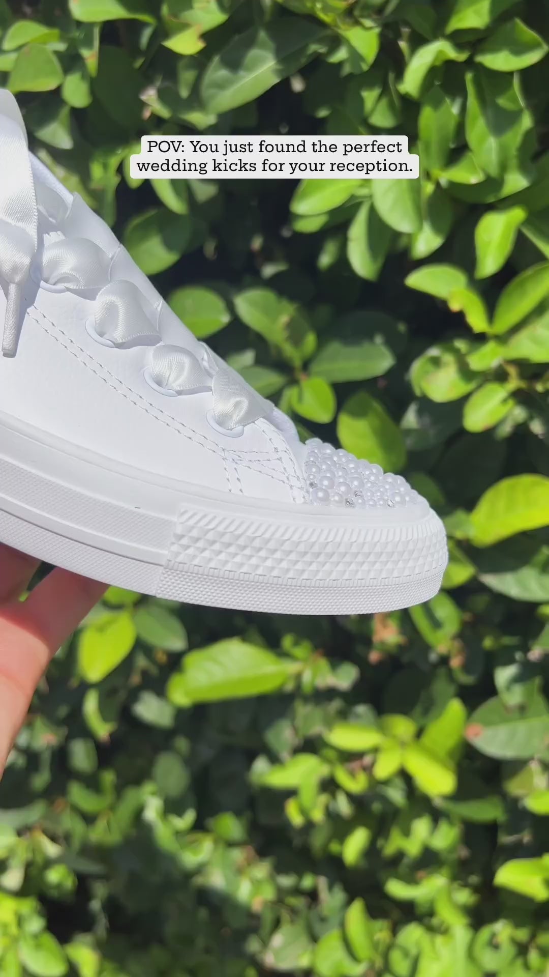 White pearl-trimmed wedding sneakers held up in a garden